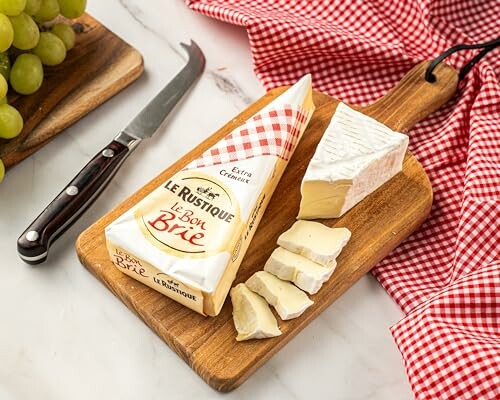 Sliced Brie cheese on a wooden board with a knife and grapes.