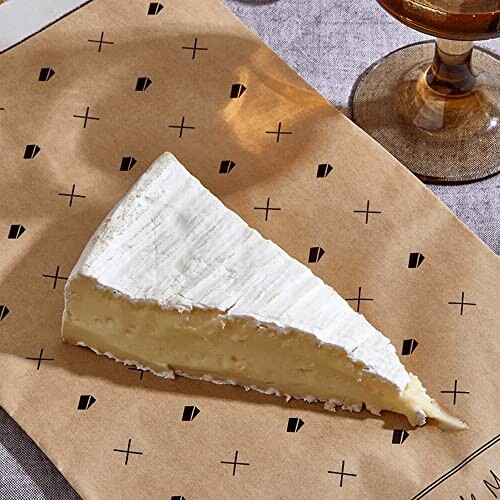 Slice of brie cheese on patterned paper with a drink nearby