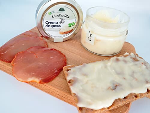 Cheese spread on cracker with cured meat on a board.