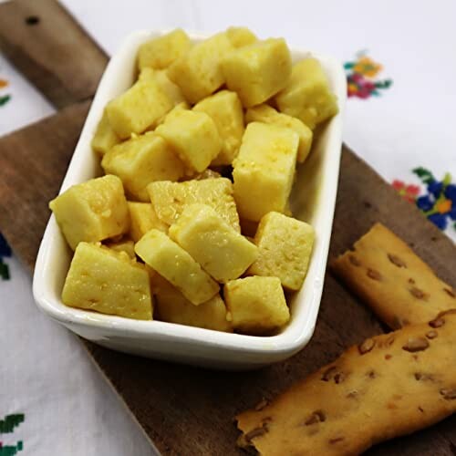 Bowl of golden cube-shaped snacks on a wooden board.