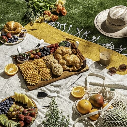 Picnic with pastries, fruits, and drinks on a blanket.